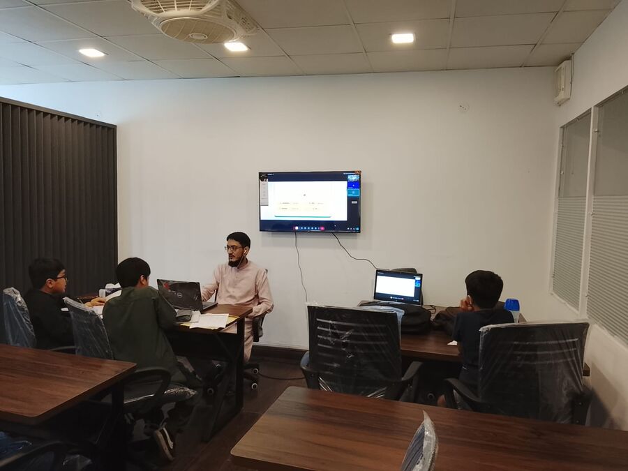 A teacher running a small class with children at laptops