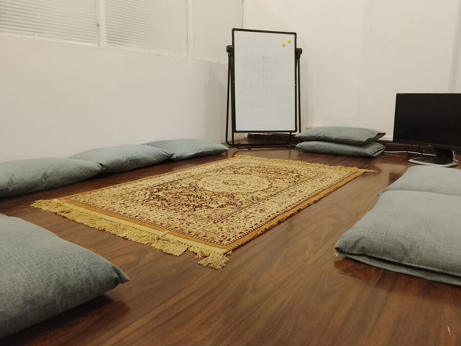 A floor-seating room with cushions, a rug and a whiteboard